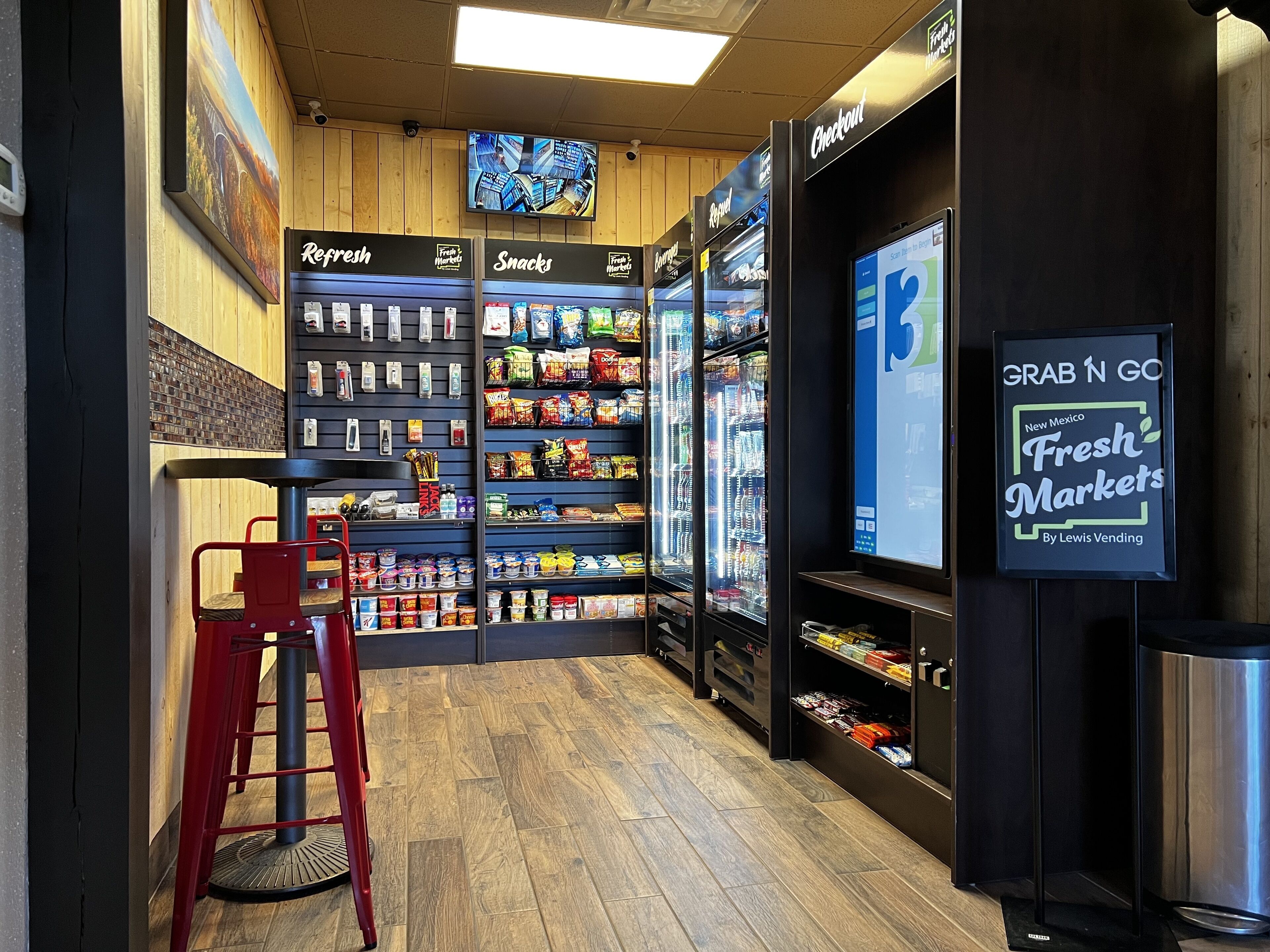 A store interior with refrigerated sections labeled 'Refreshed' and 'Snacks', a checkout area, and a 'Grab n Go' sign for New Mexico Fresh Markets.