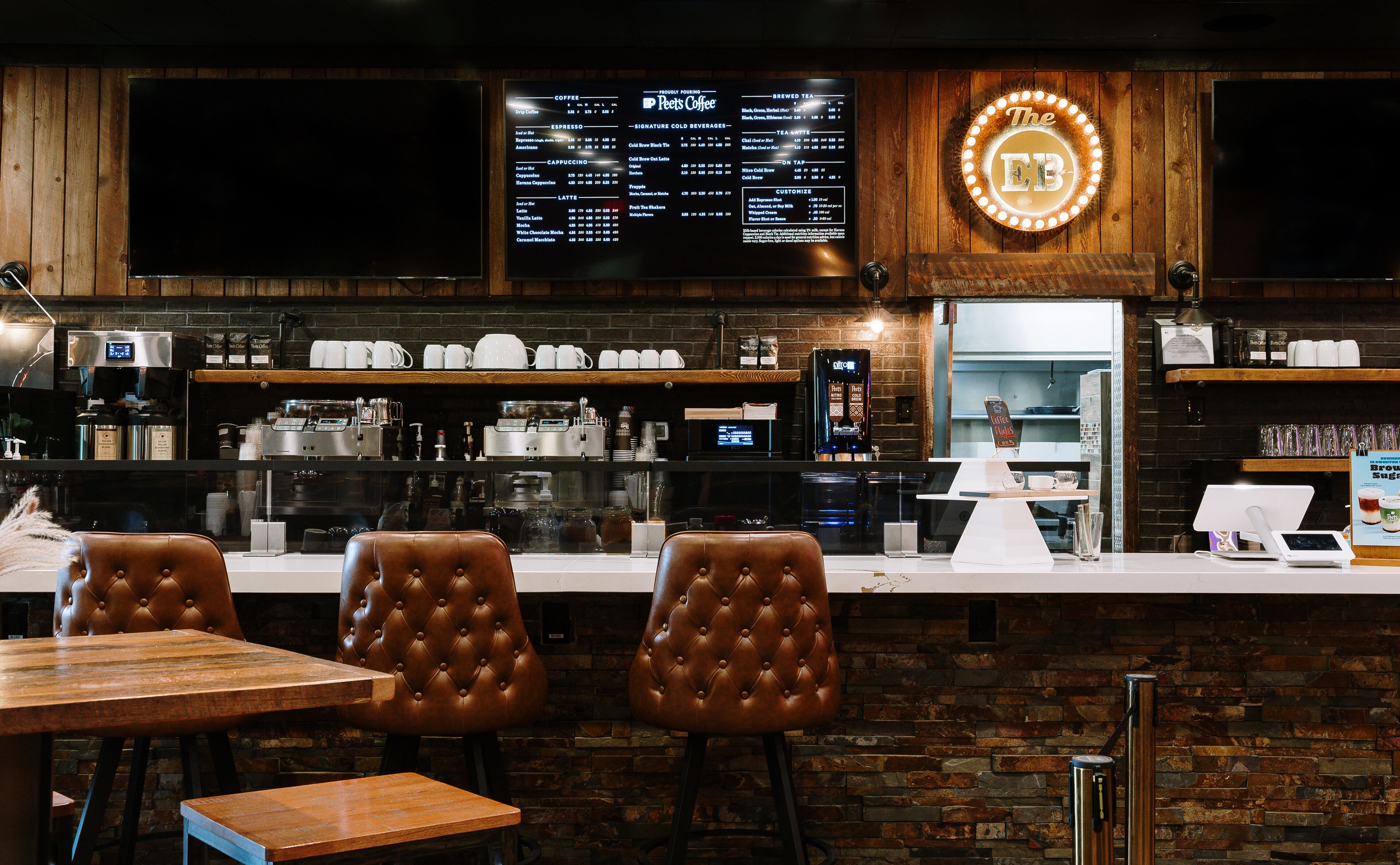 A coffee shop interior with a menu board, espresso machines, and leather chairs.