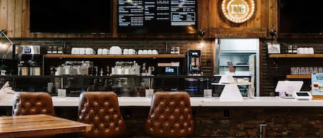 L’intérieur d’un café, avec un tableau affichant le menu, des machines à expresso et des fauteuils en cuir.