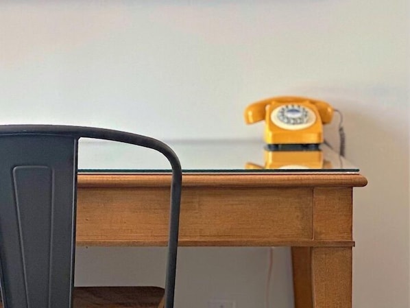 Una mesa de madera con tapa de vidrio y un teléfono giratorio amarillo antiguo encima.