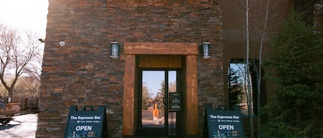 A brick building with a wooden door and two signs indicating The Espresso Bar is open.