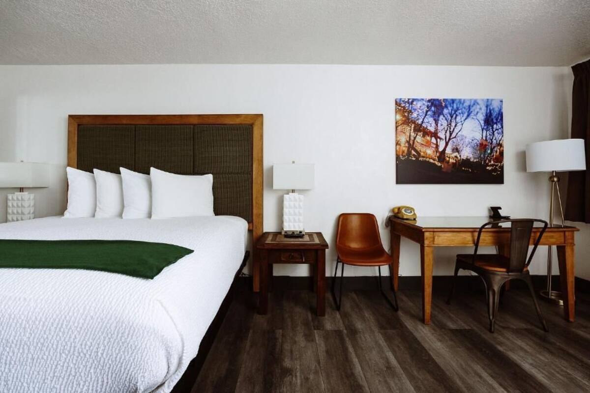 A hotel room with a large bed, a desk, two chairs, a small table, and a wall-mounted lamp.