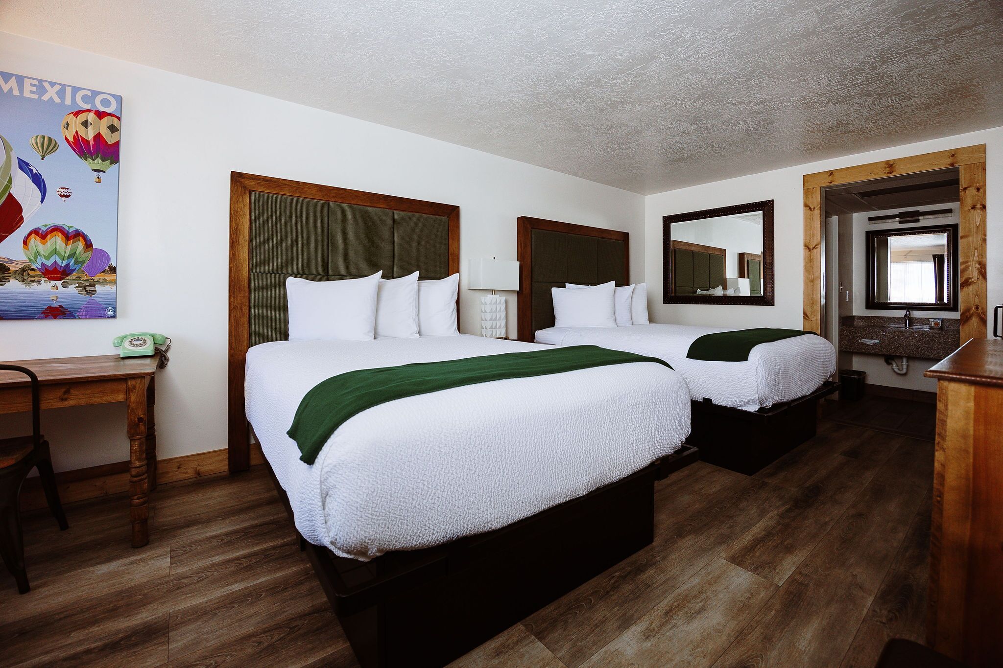 Quarto de hotel com duas camas, uma escrivaninha, telefone e um quadro com balões de ar quente.