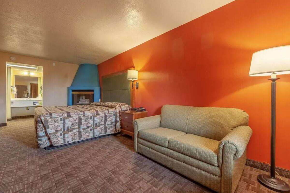 A hotel room with a bed, a sofa, a lamp, and a fireplace.