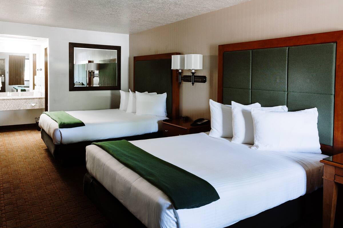 A hotel room with two beds, a large mirror, bedside lamps, and a wooden headboard.