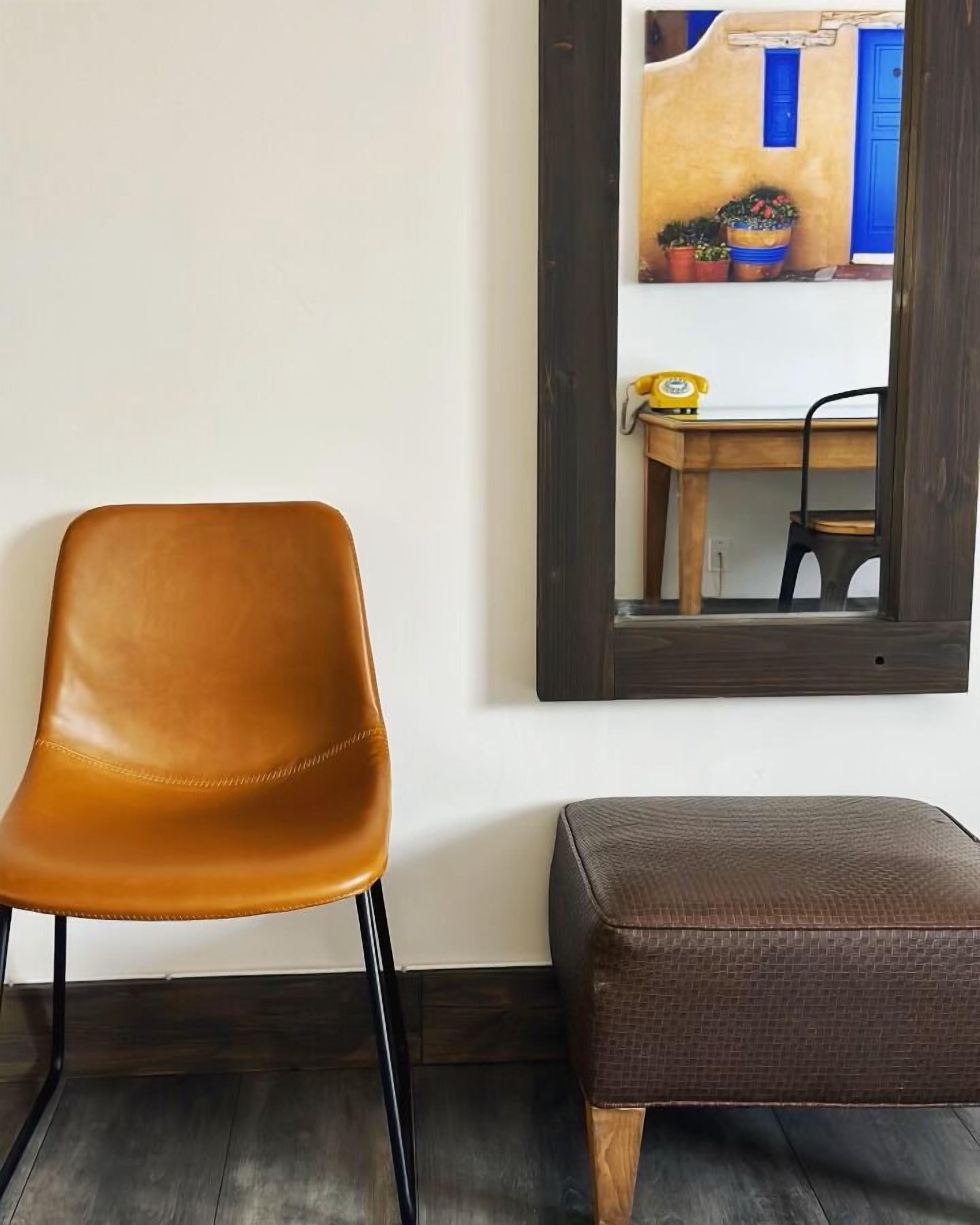 A room with a brown leather chair, a wooden bench, and a mirror reflecting a yellow wall with blue doors and potted plants.