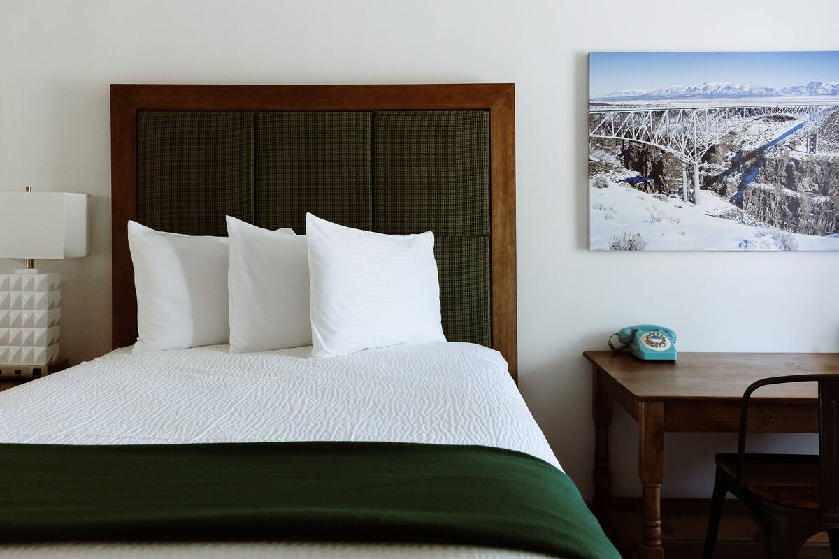A neatly made bed with a wooden headboard, a bedside table with a lamp, and a chair.