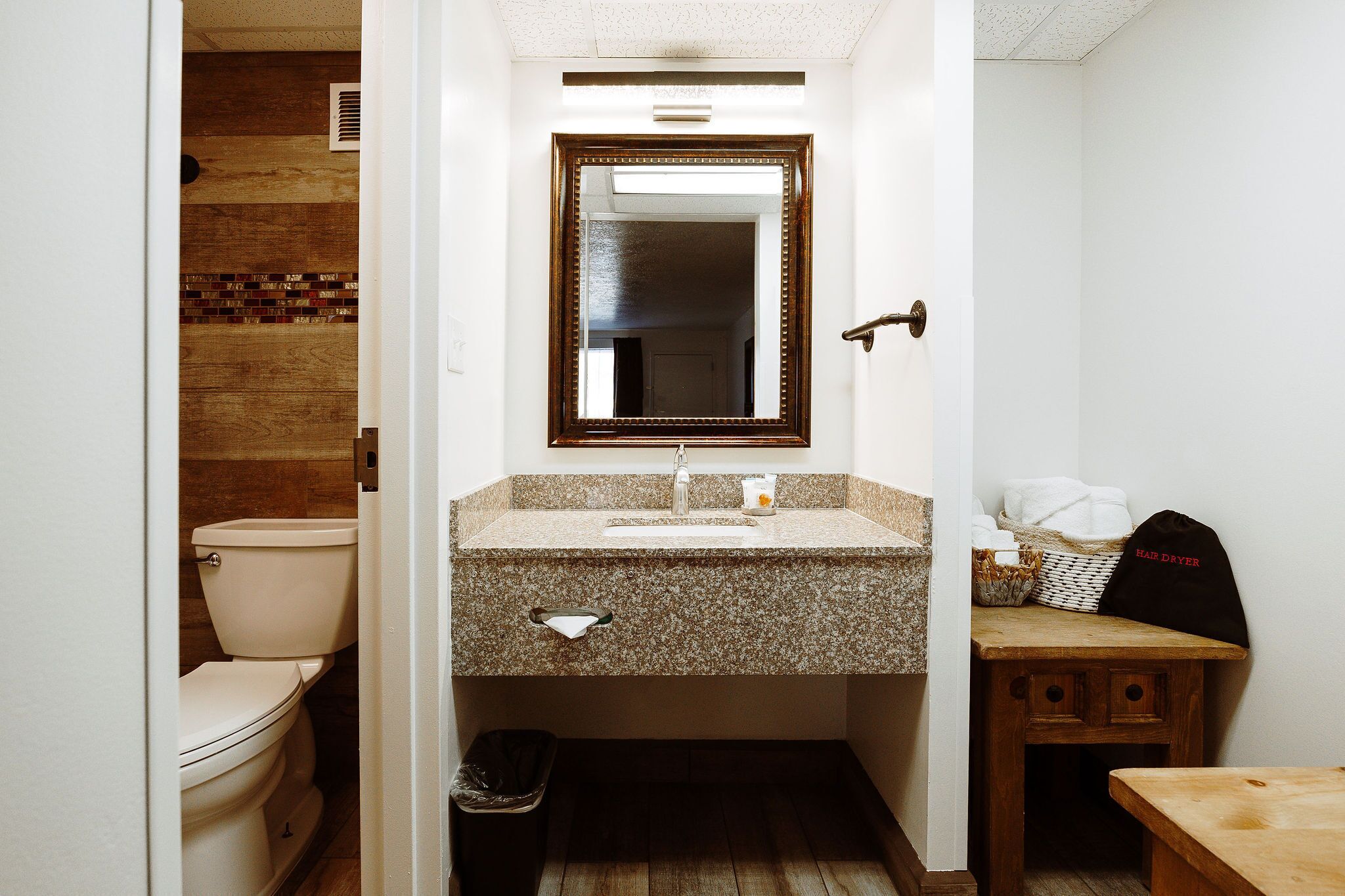 A bathroom with a toilet, sink, mirror, and a small wooden table.