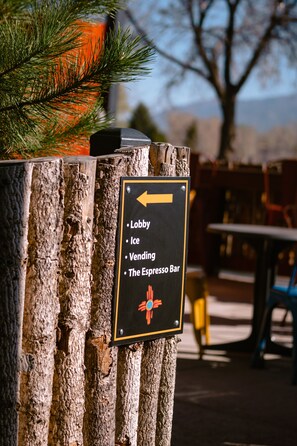 A sign on a wooden post with a list of amenities including a lobby, ice, vending, and the espresso bar. - Taos Valley Lodge (Taos)