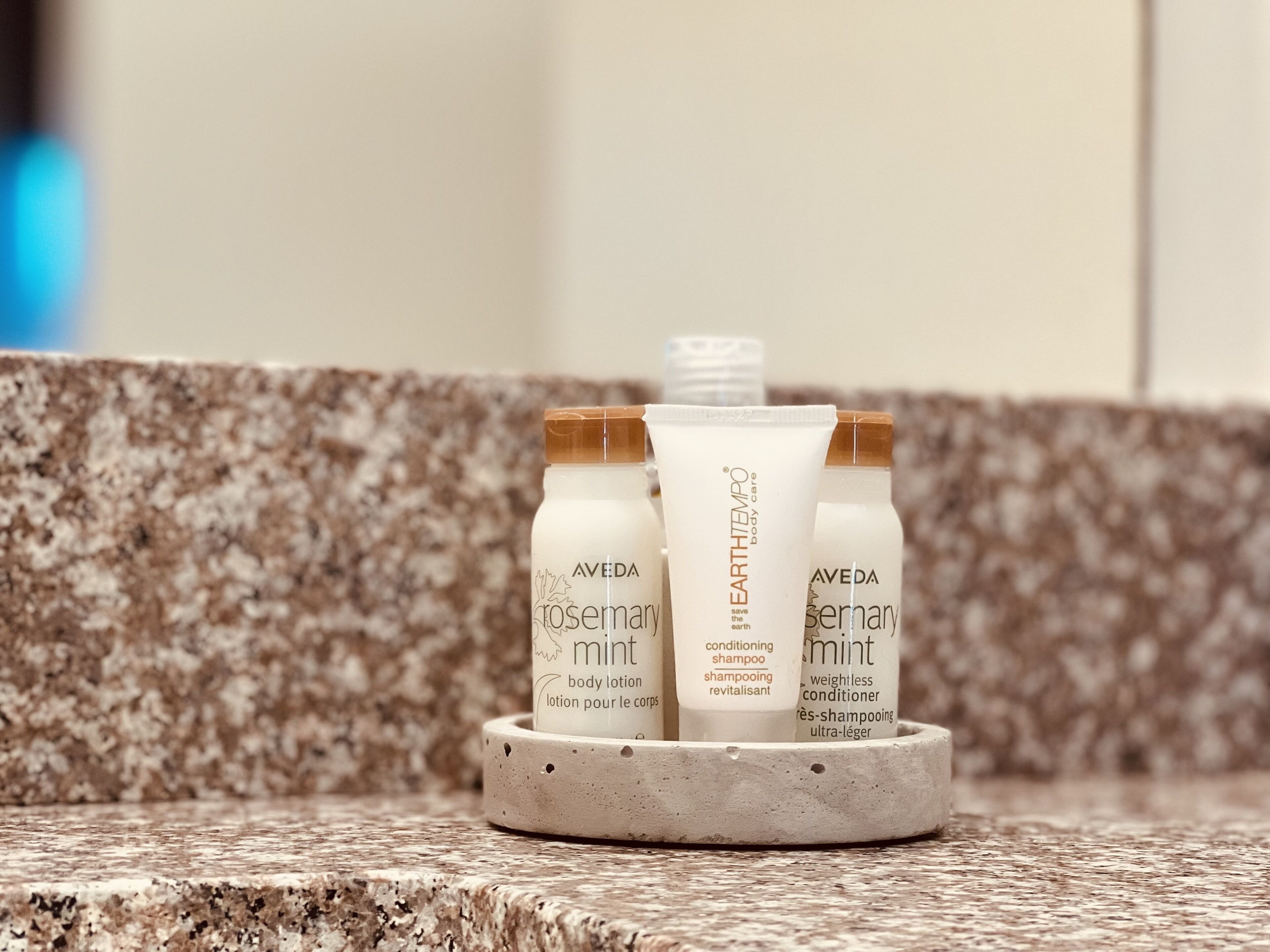 Three bottles of Aveda body care products on a granite countertop.