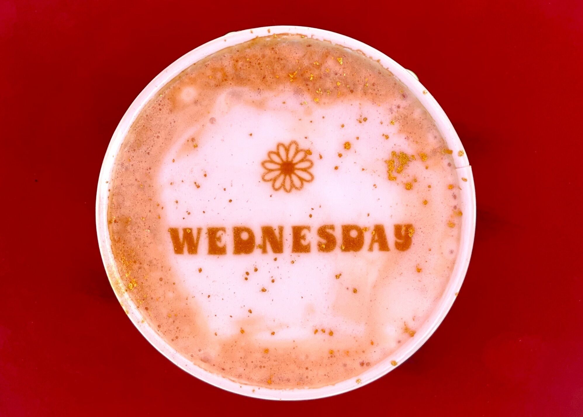 Eine Kaffeetasse mit der Aufschrift "WEDNESDAY", einem Blumenmuster und goldenen Flocken.