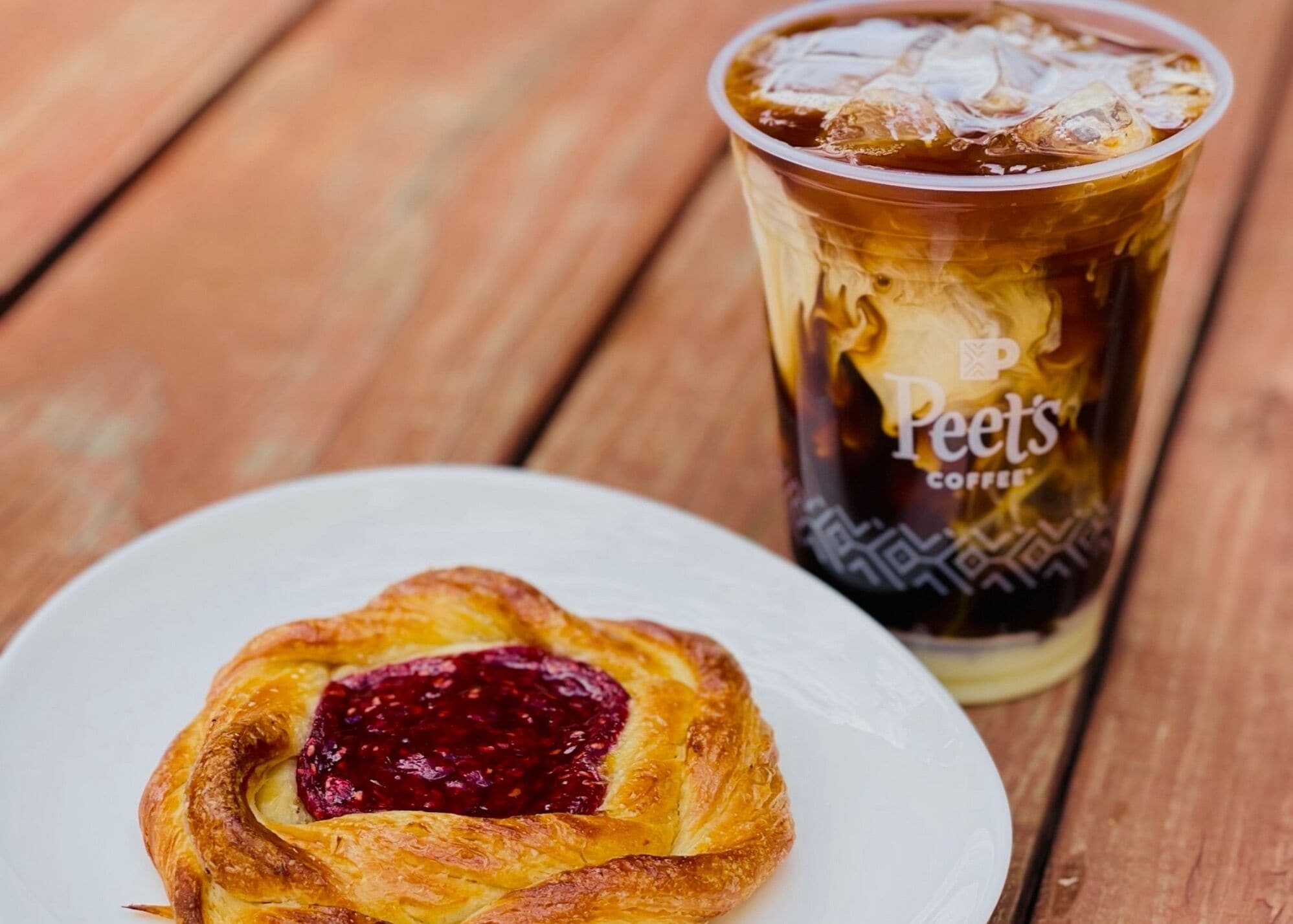 A pastry with a berry filling on a white plate and a glass of iced coffee with a label reading "Peet's Coffee".