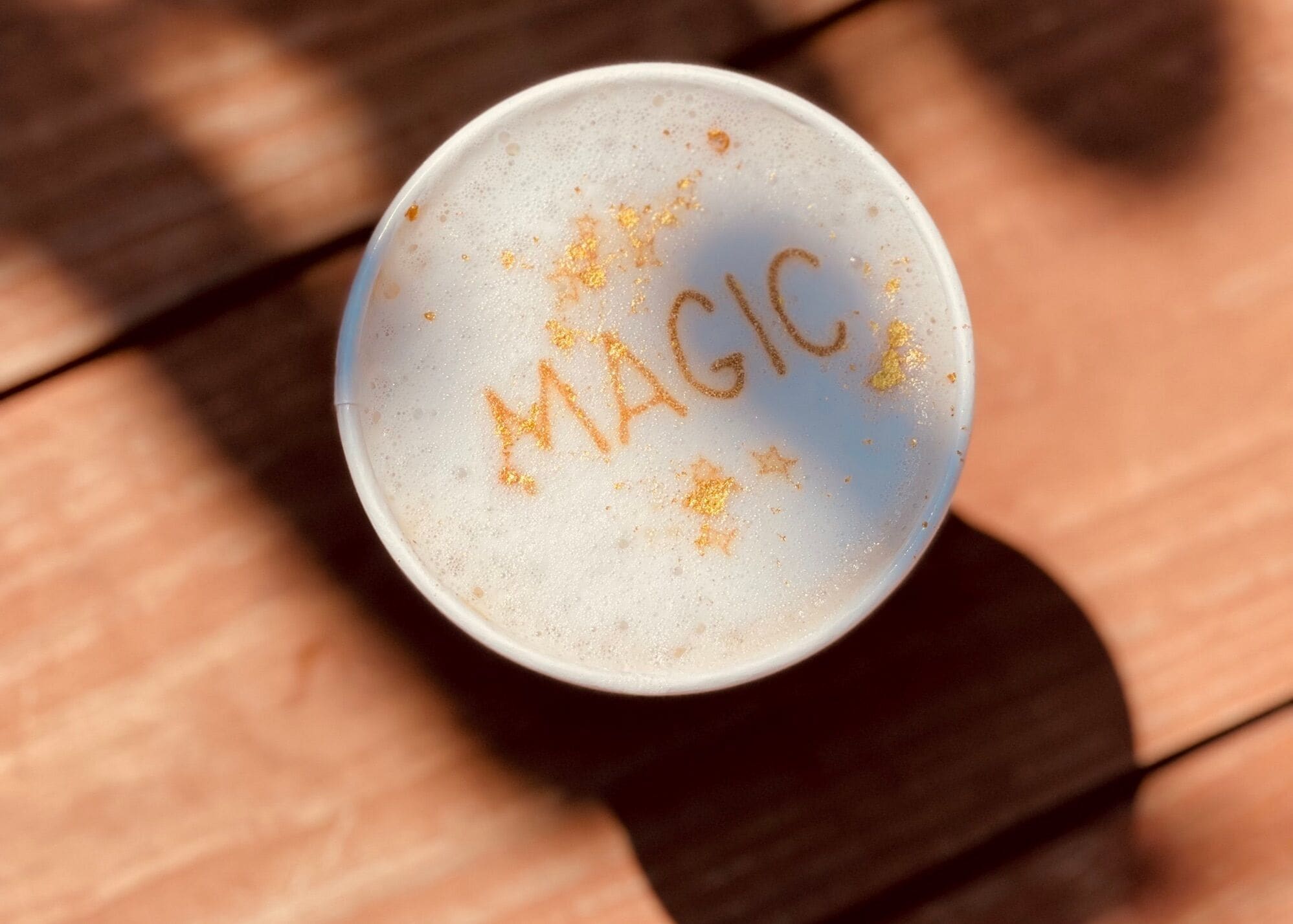 A white cup with the word "MAGIC" written on it, placed on a wooden surface.