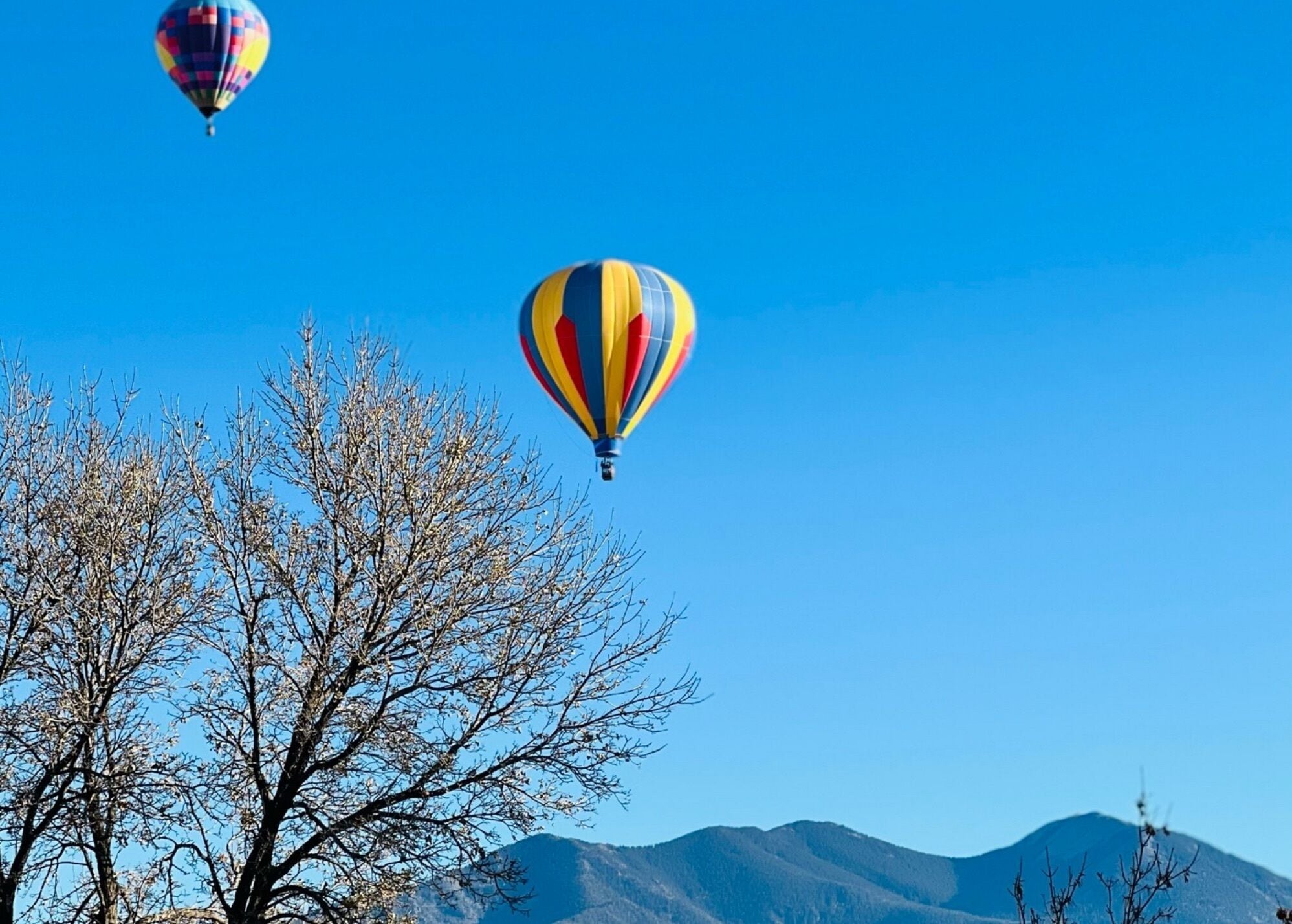 Zwei Heißluftballons in wolkenlosem, blauem Himmel mit einem Bergmassiv im Hintergrund.