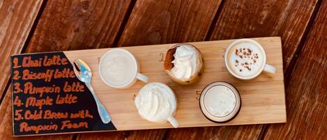 A wooden board with a list of five latte drinks and a spoon.