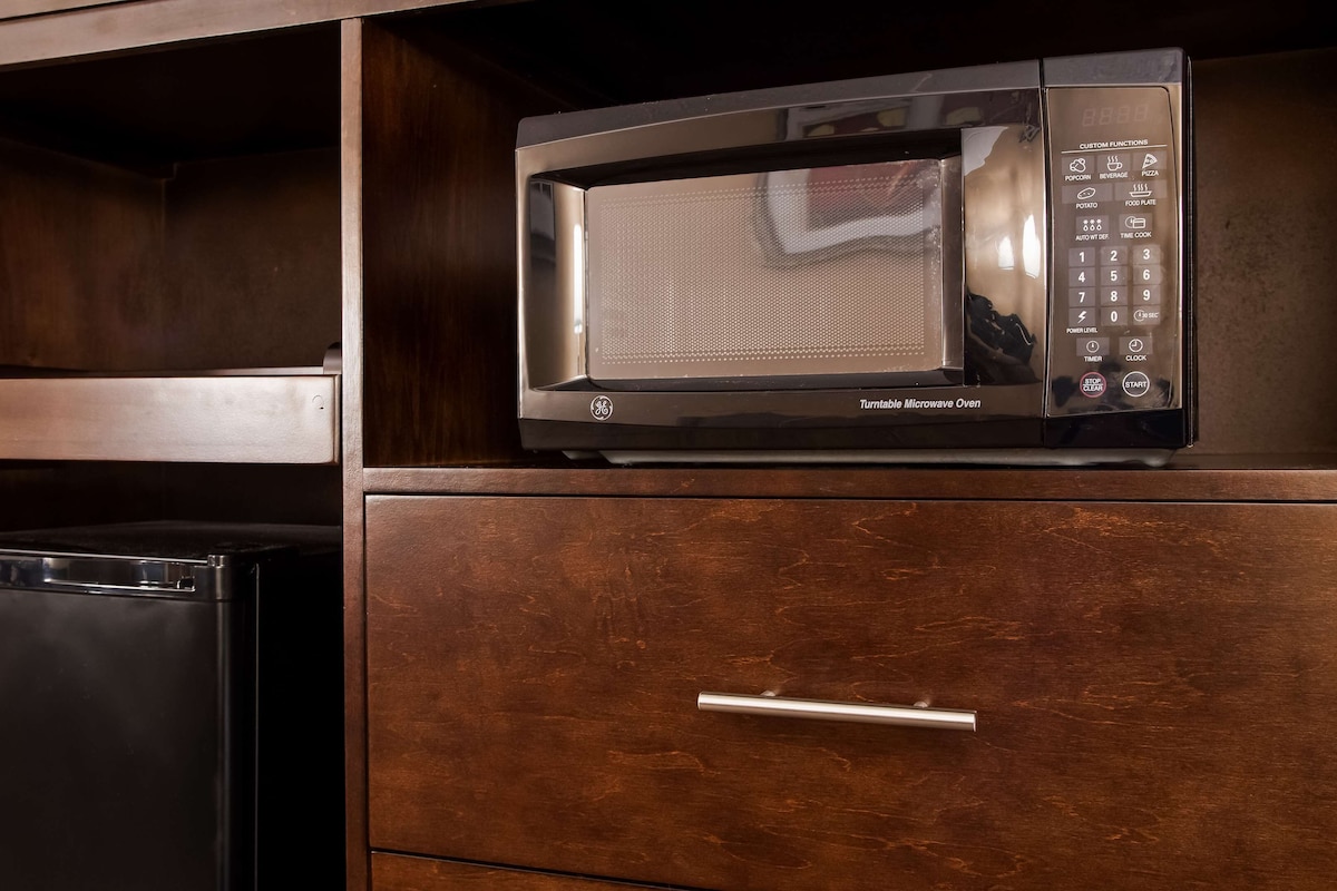 A kitchen with a black refrigerator, a microwave oven, and a wooden cabinet with a drawer.