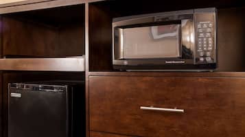 A kitchen with a black refrigerator, a microwave oven, and a wooden cabinet with a drawer.
