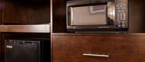 A kitchen with a black refrigerator, a microwave oven, and a wooden cabinet with a drawer.