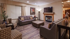 A modern living room with a grey sofa, patterned armchairs, a fireplace, and a flat-screen TV. - Best Western Crossroads Of The Bluffs (Council Bluffs)