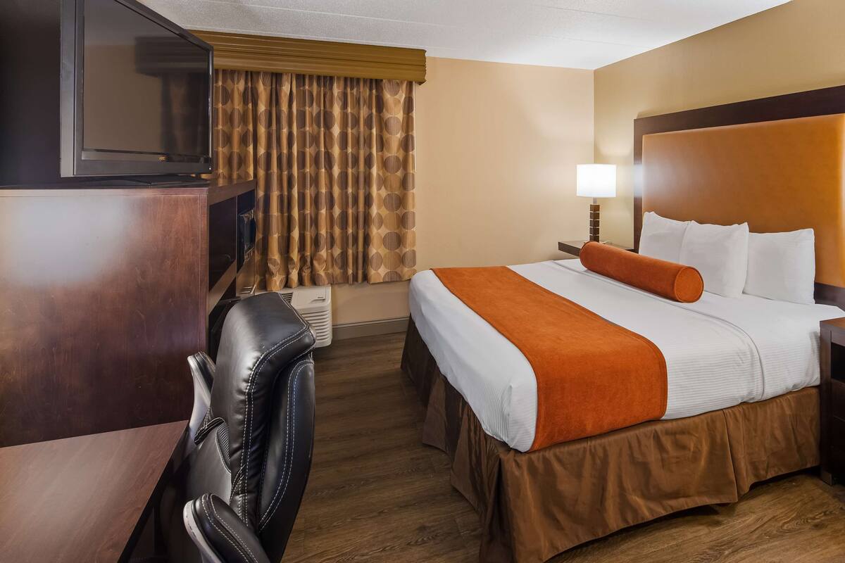 A hotel room with a large bed, two bedside lamps, a TV, a leather chair, and a wooden floor.