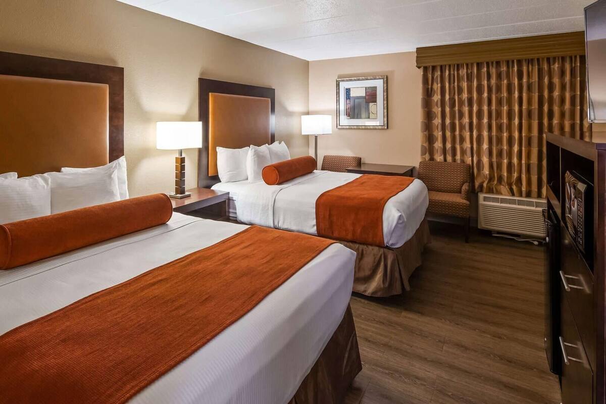 A hotel room with two beds, a desk, a chair, a TV, and a mirror.