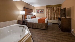 A hotel room with a large bathtub, a bed with white and brown bedding, a bedside table with a lamp, a TV, and a window with curtains. - Best Western Crossroads Of The Bluffs (Council Bluffs)