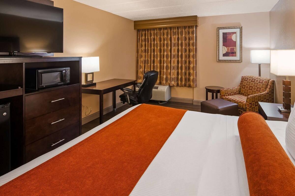 A hotel room with a large bed, a desk, a chair, a TV, and a lamp.