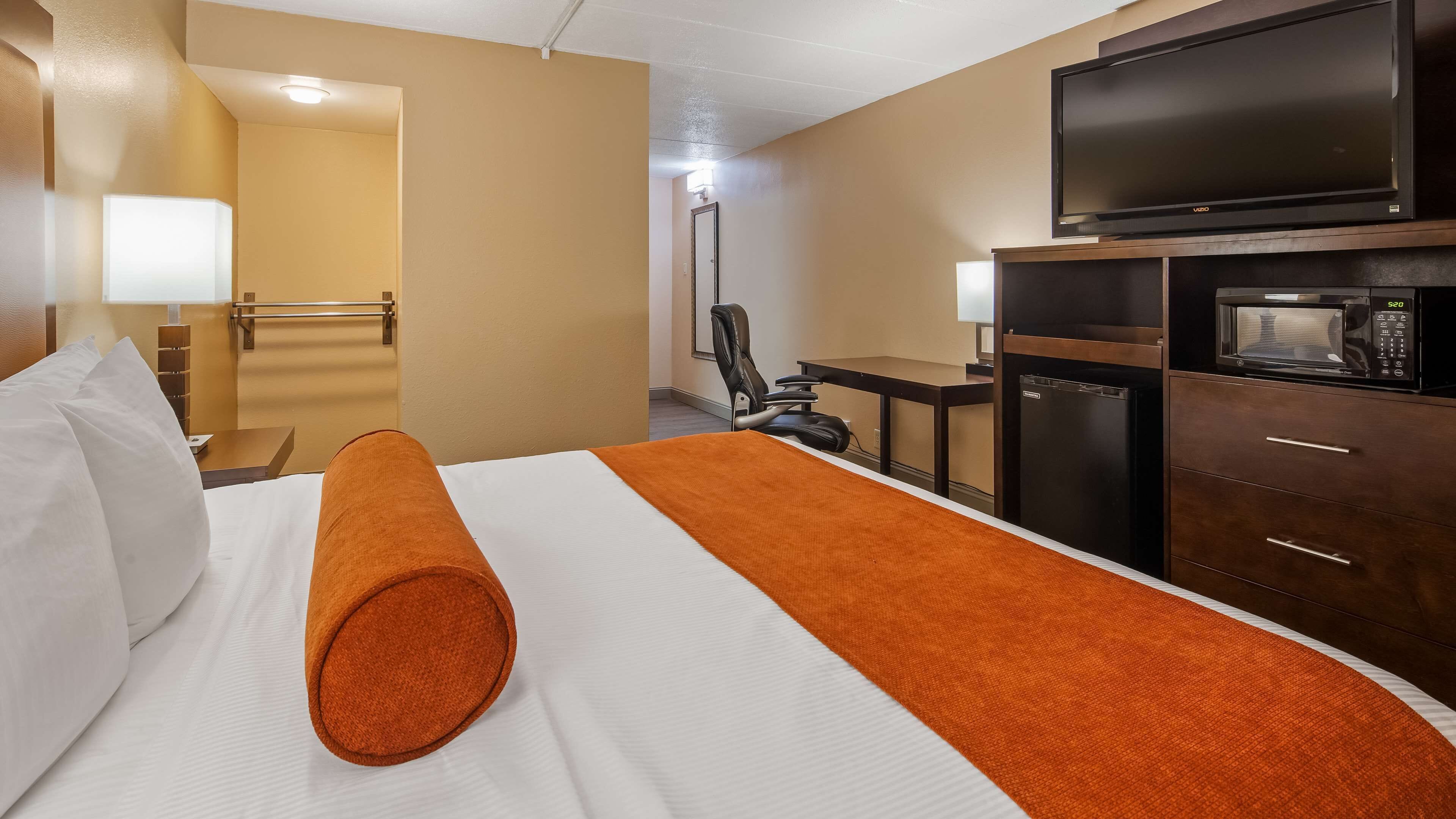 Habitación de hotel con cama, escritorio, silla, televisor, microondas y refrigerador.