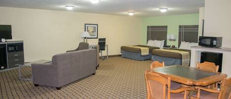 Una habitación de hotel con sofá, cama, mesa de comedor con sillas, televisión y microondas.