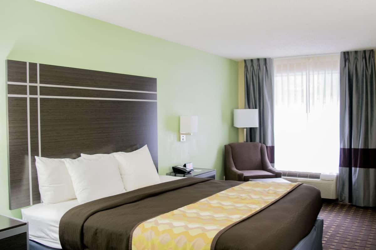 A hotel room with a large bed, a chair, a desk, and a window with curtains.