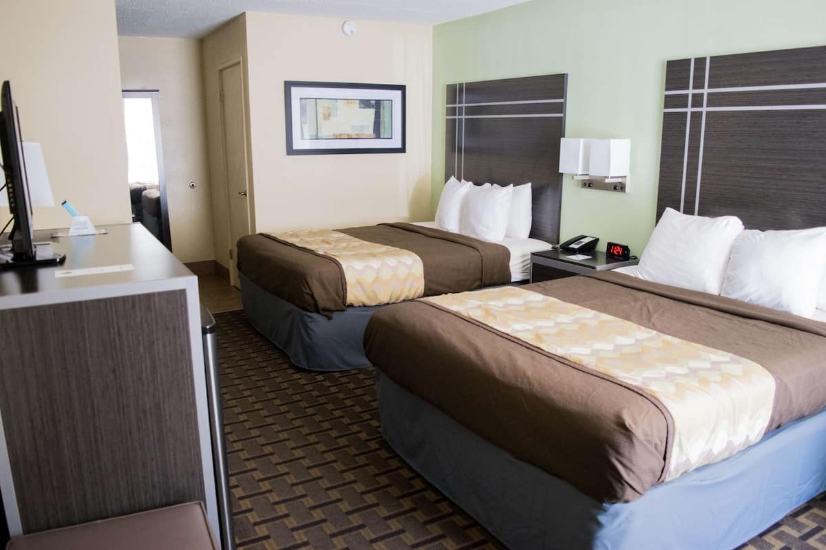 A hotel room with two beds, a desk, and a chair. There is a framed picture on the wall and a clock on the nightstand.