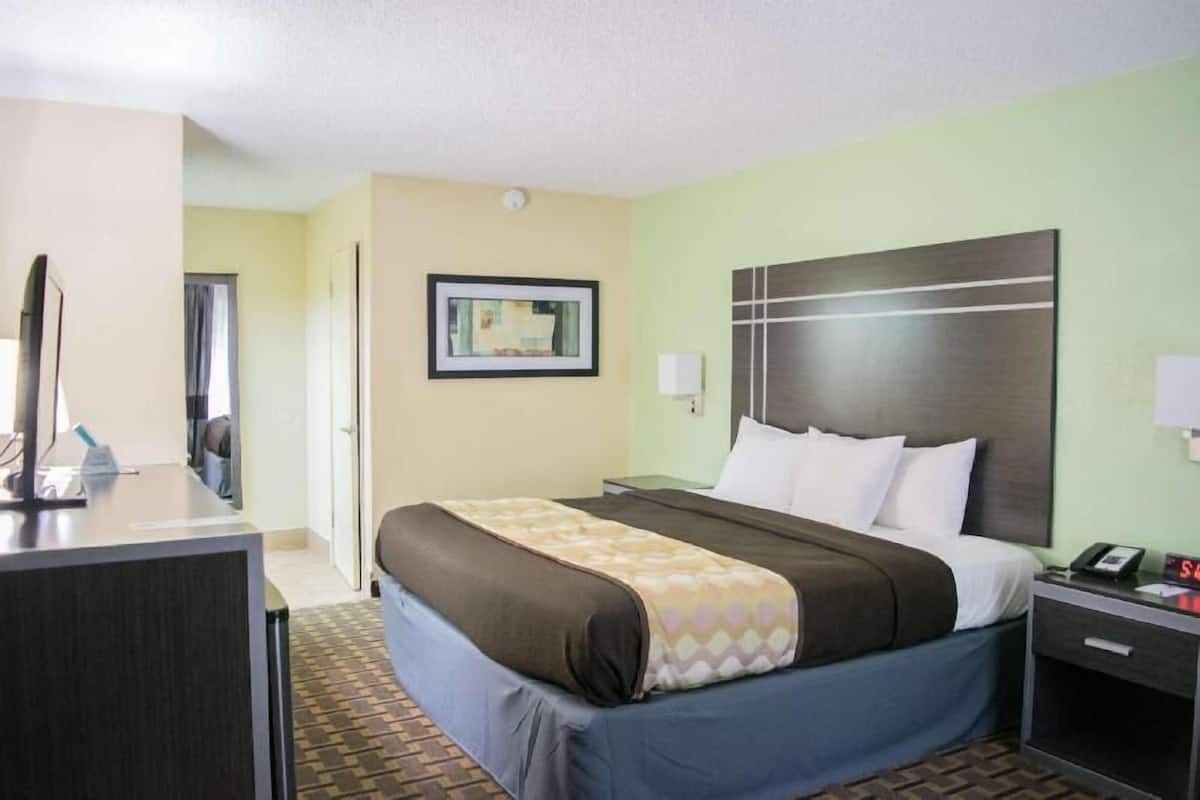 A hotel room with a bed, bedside table, desk, and a framed picture on the wall.
