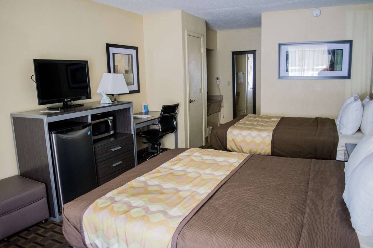 A hotel room with two beds, a desk with a computer, a television, and a refrigerator.