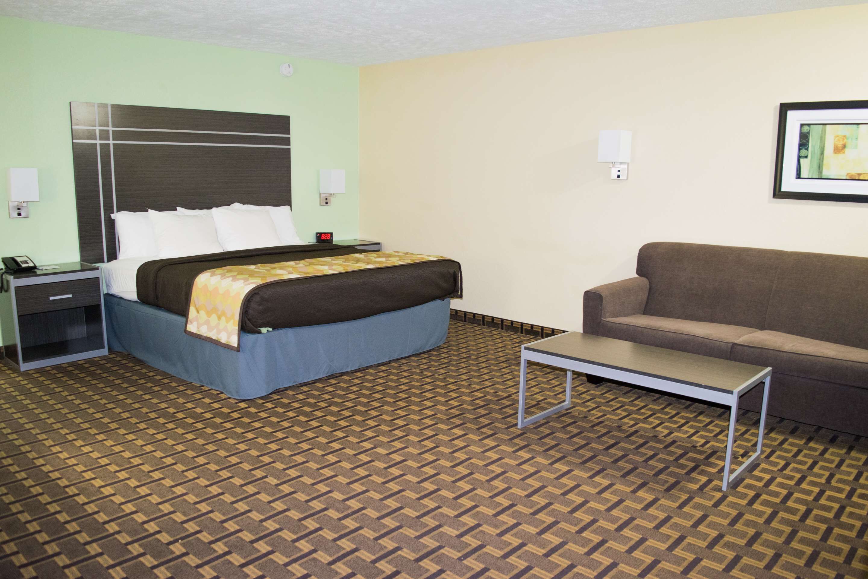 A hotel room with a bed, a sofa, a nightstand, and a table.