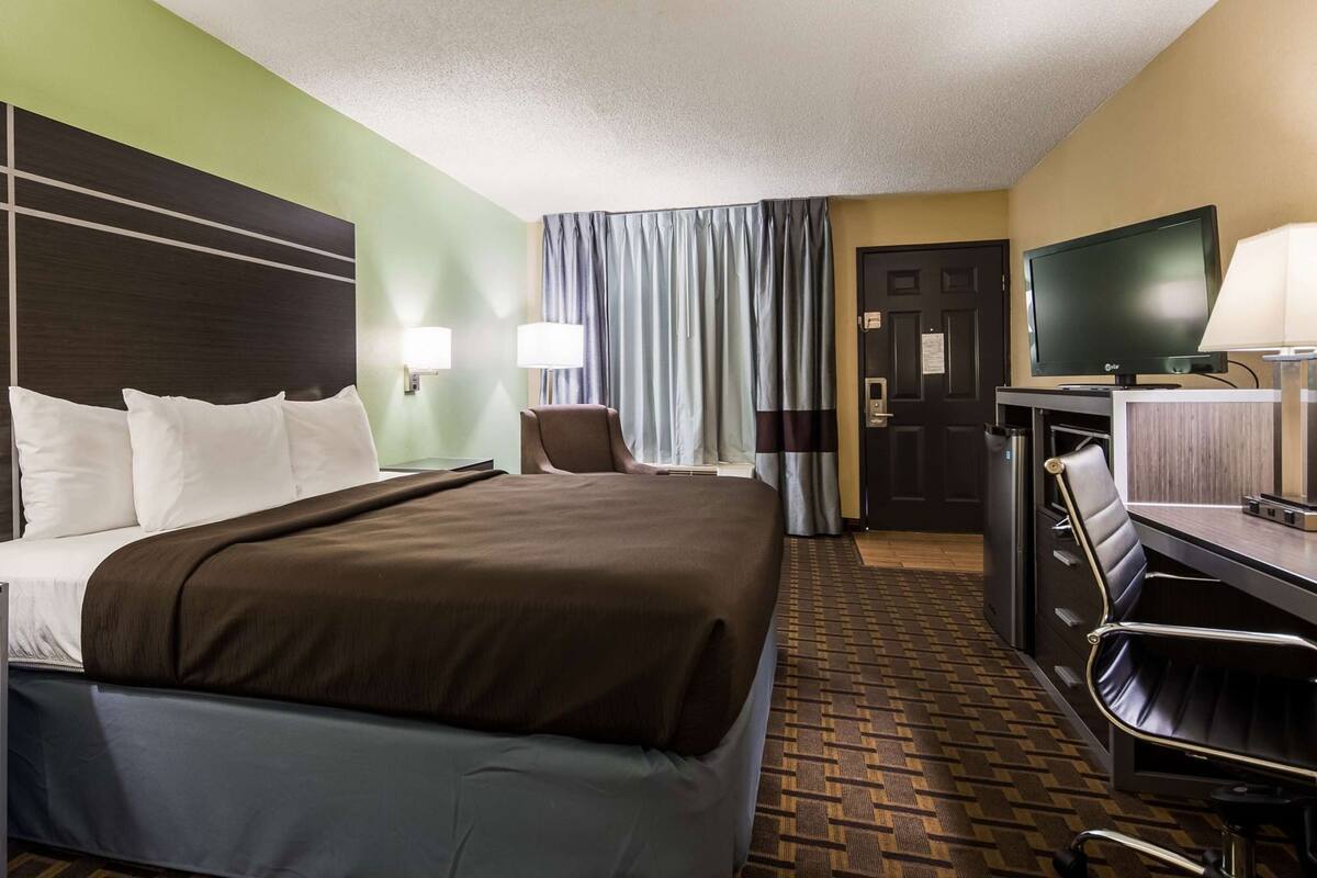 A hotel room with a bed, a desk, a chair, a television, and a door.