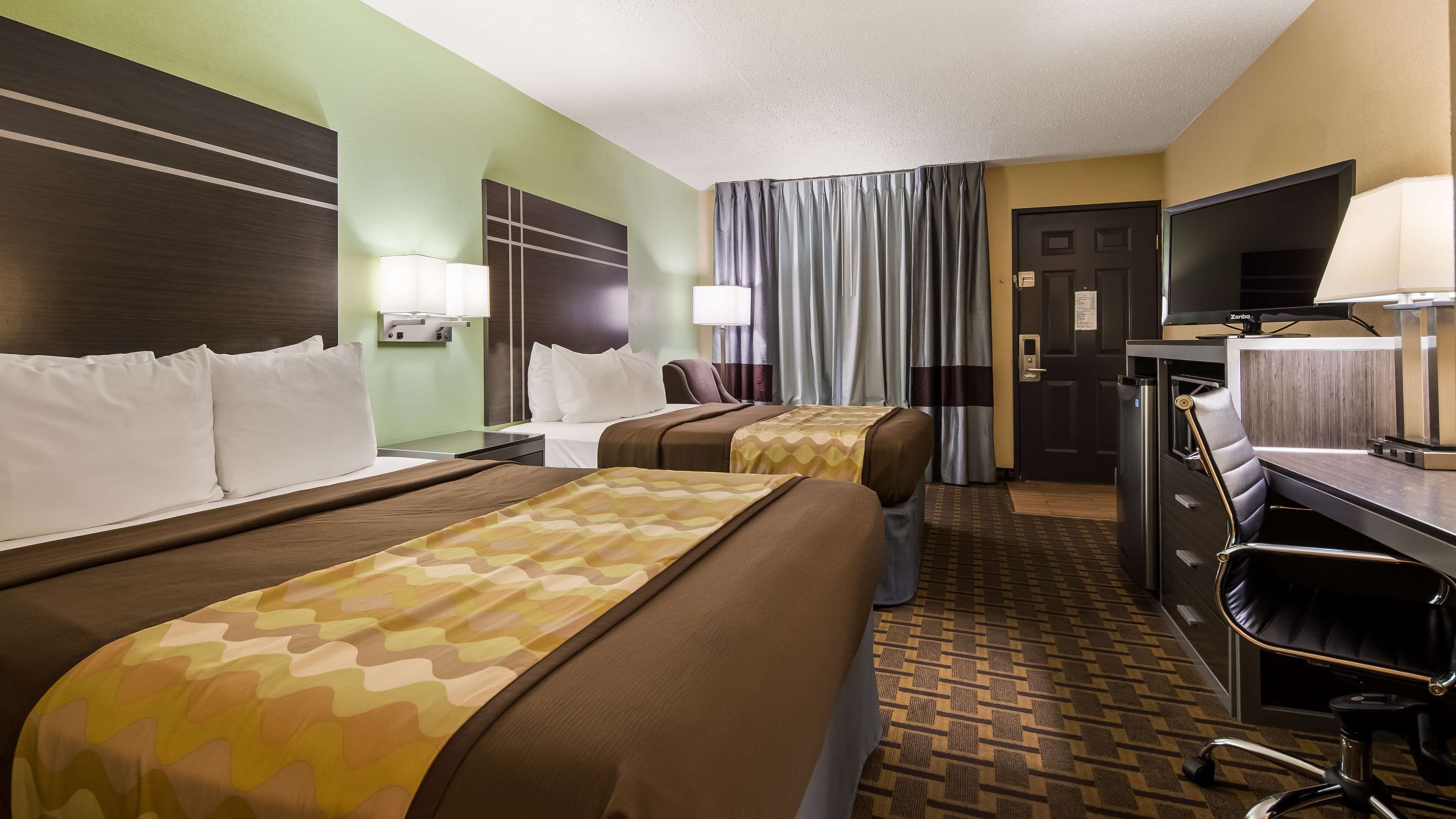 A hotel room with two beds, a desk, a chair, a television, and a bathroom.