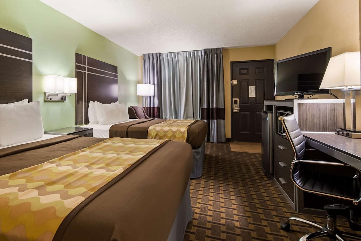 A hotel room with two beds, a desk with a chair, a television, and a door.