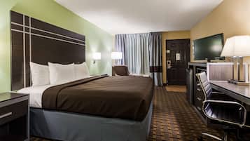 A hotel room with a large bed, a desk with a chair, a television, and a lamp.