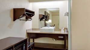 Een hotelbadkamer met een wastafel, spiegel, handdoekhouder en een klein kastje.