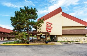Ein Red Roof Inn mit rotem Dach, beige farbenen Außenwänden und einer überdachten Außenberecks mit Blumentöpfen.