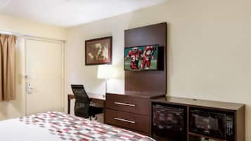 Quarto de hotel com cama, escrivaninha, cadeira, televisão e micro-ondas.