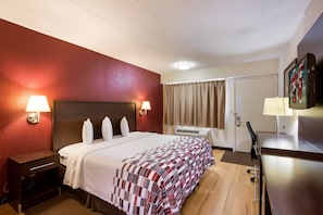 A hotel room with a large bed, two bedside lamps, a desk with a chair, and an air conditioning unit. - Red Roof Inn Grand Rapids Airport (Grand Rapids)