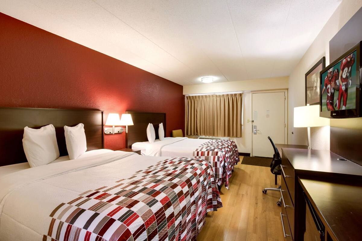 Une chambre d’hôtel avec trois lits, une télévision, un bureau et une porte.