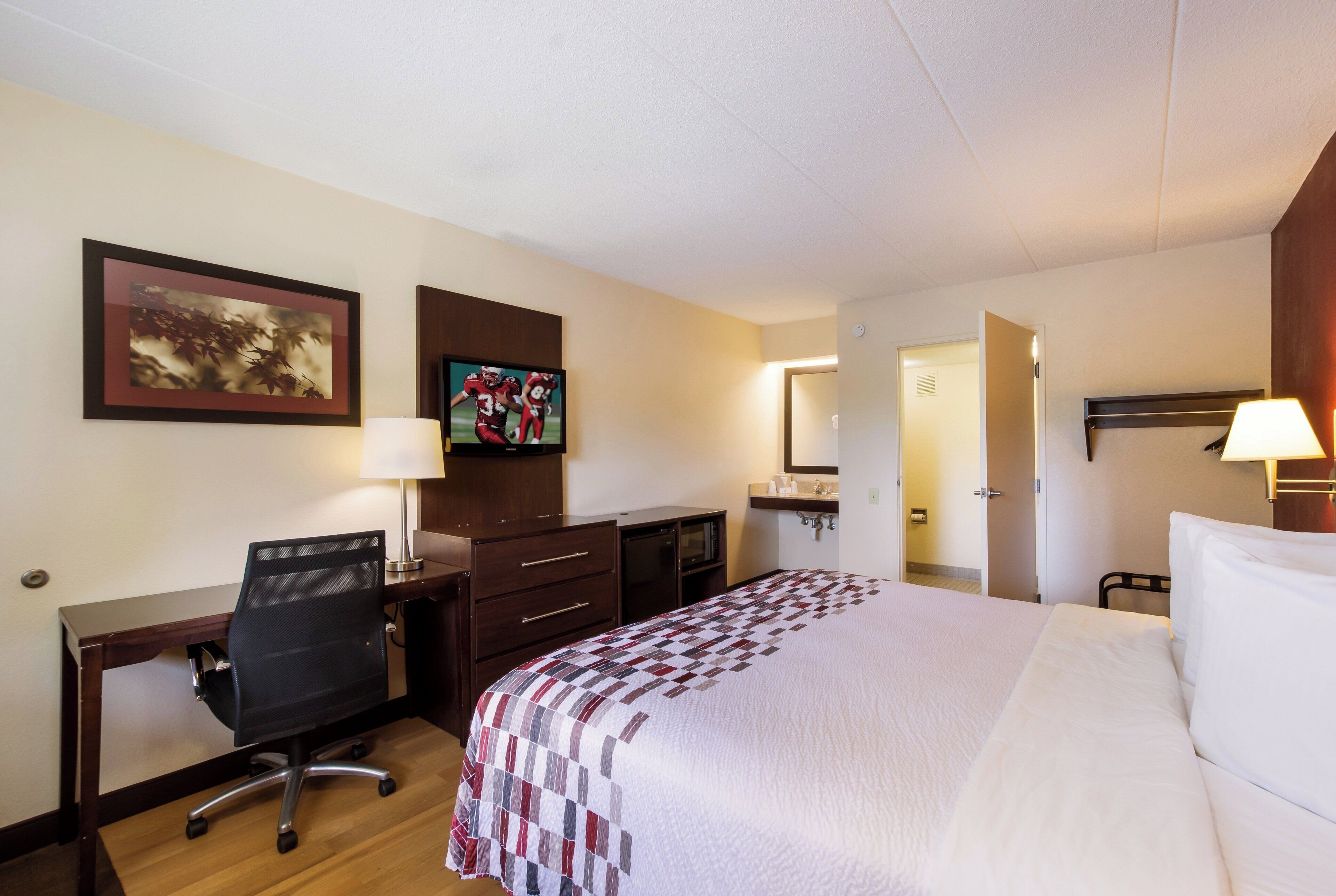 A hotel room with a bed, desk, chair, television, and a bathroom visible through an open door.