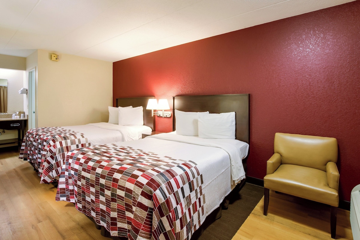 A hotel room with two beds, a chair, a nightstand, and a lamp.