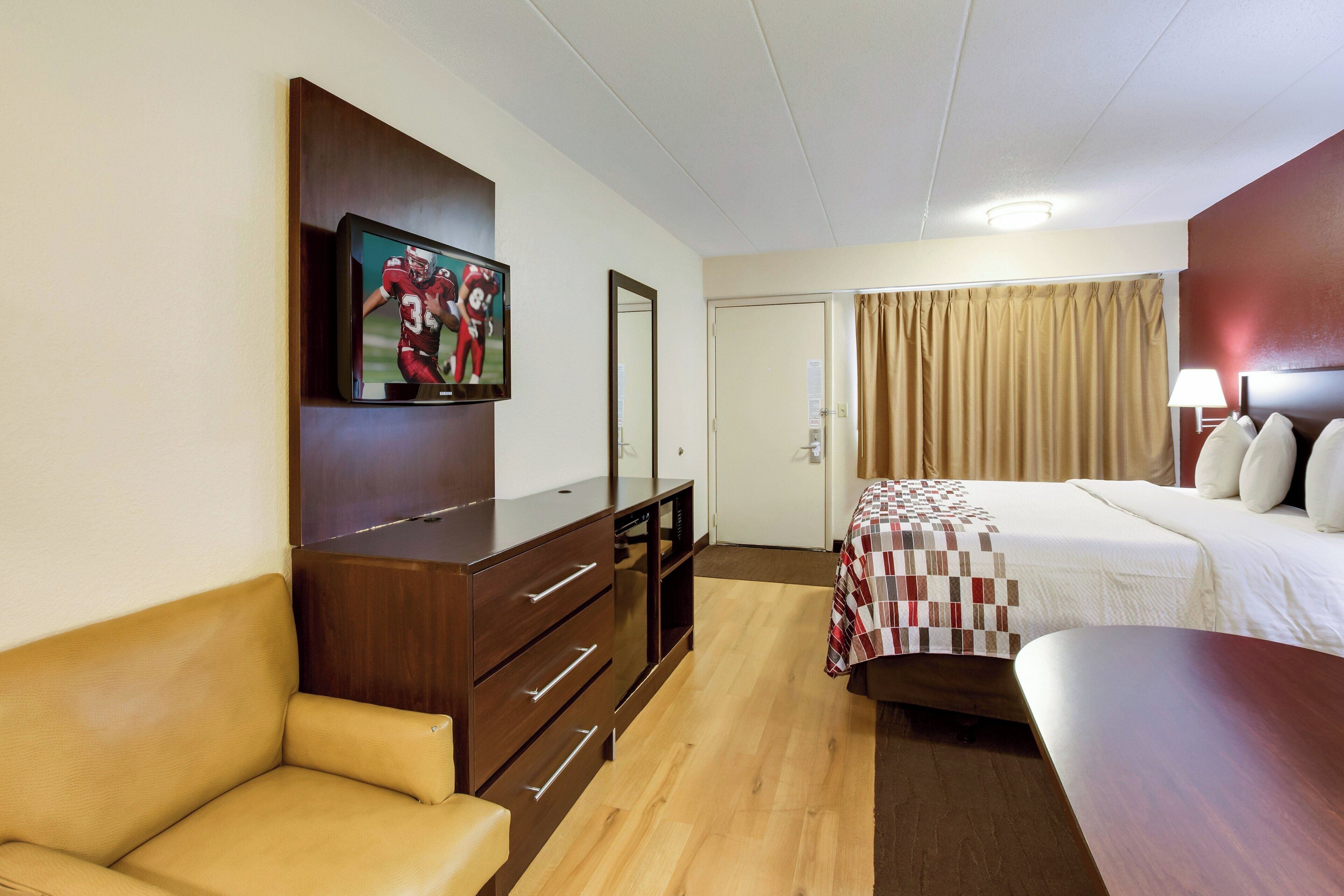 Habitación de hotel con una cama, televisión montada en la pared, un escritorio y una silla.