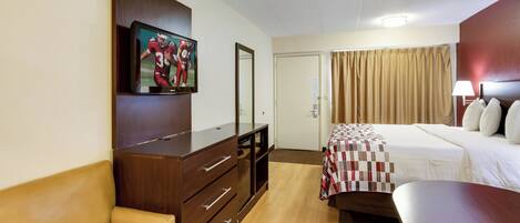 Habitación de hotel con una cama, televisión montada en la pared, un escritorio y una silla.