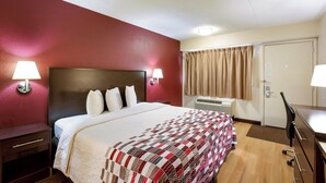 Ein Hotelzimmer mit einem Bett, Nachttischlampen, einem Schreibtisch und einem Fenster mit Vorhängen.