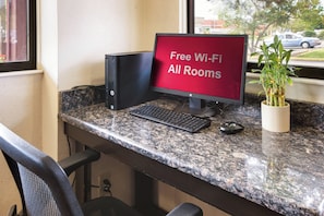 Ein Arbeitsplatz mit einem Desktop-Computer, Tastatur und einem Monitor, der 'Kostenloses WLAN in allen Zimmern' anzeigt.