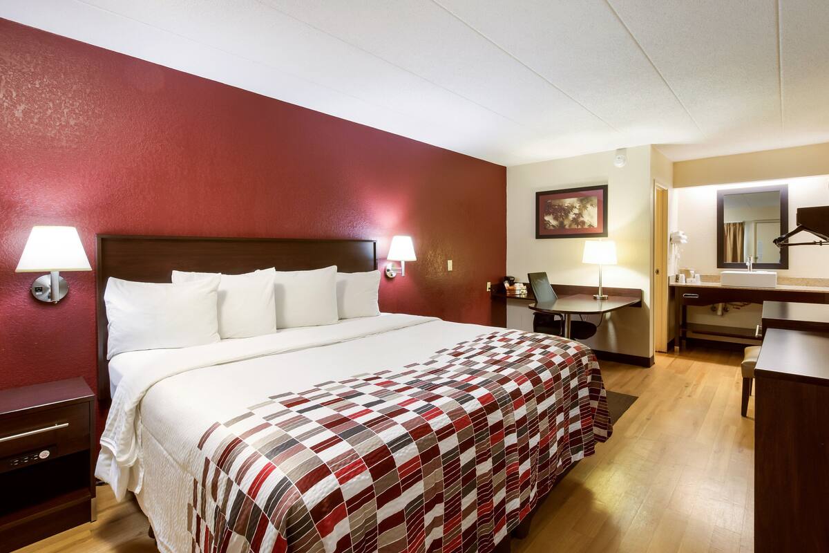Une chambre d’hôtel avec un grand lit, un bureau, une chaise, un miroir et une table de chevet.